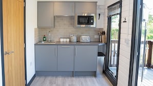 A modern kitchen with grey cabinets, a microwave, and a toaster. There is a wooden door on the left and a sliding glass door on the right. - Beautiful Open Plan Lakeside Lodge, Shearsby (Lutterworth)