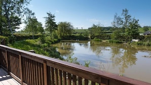 A wooden deck overlooking a calm pond surrounded by lush greenery. - Beautiful Open Plan Lakeside Lodge, Shearsby (Lutterworth)