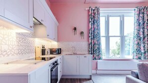 Et moderne køkken med hvide skabe, indbygget ovn og et vindue med blomstrede gardiner.