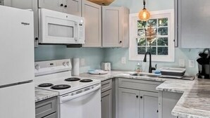 A kitchen with white cabinets, a white stove, a microwave, and a hanging light fixture.