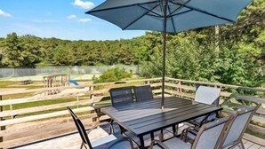 A deck with a table and chairs, overlooking a lake and a fenced area with a pool.