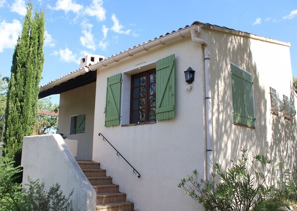 A two-story house with a staircase leading to the upper floor, green shutters on the windows, and a white exterior.