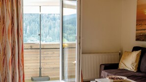 A living room with a wooden ceiling, a sliding glass door leading to a balcony, a brown sofa, a small table with a bowl, and a patterned rug. - Vacation apartment Mountain View 2 (Spital am Pyhrn)