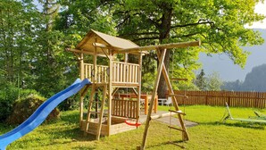 A wooden play structure with a slide and swings in a grassy backyard. - Vacation apartment Mountain View 2 (Spital am Pyhrn)