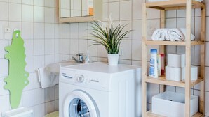 A modern bathroom with a washing machine, a shelf with towels, a plant, and a green bath mat. - Vacation apartment Mountain View 2 (Spital am Pyhrn)