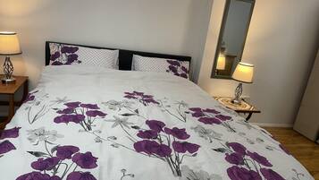 A neatly made bed with a floral bedspread, two bedside tables with lamps, and a mirror on the wall.