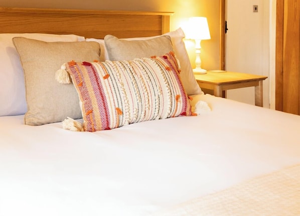 A neatly made bed with two pillows, one plain and one with a striped pattern, in a room with a wooden headboard and a bedside table with a lamp.