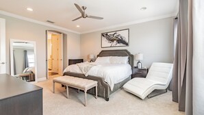 Ein Schlafzimmer mit Bett, Nachttischen, einem Sessel, einer Bank, einem Deckenventilator und einem Bild an der Wand.