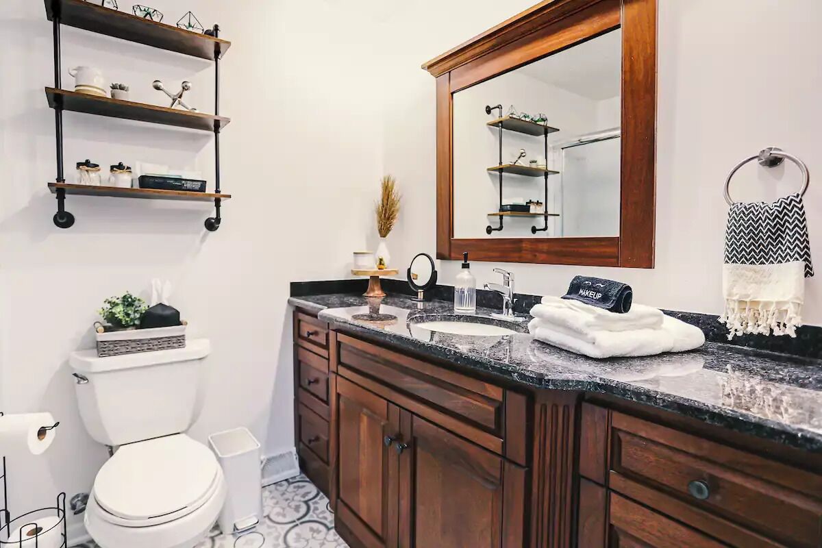 Un baño con inodoro, lavamanos, tocador, armarios de madera y estantes con artículos de aseo.