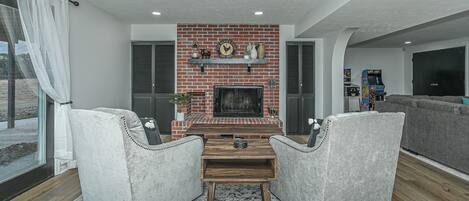 A living room with a brick fireplace, two armchairs, a coffee table, and a television.