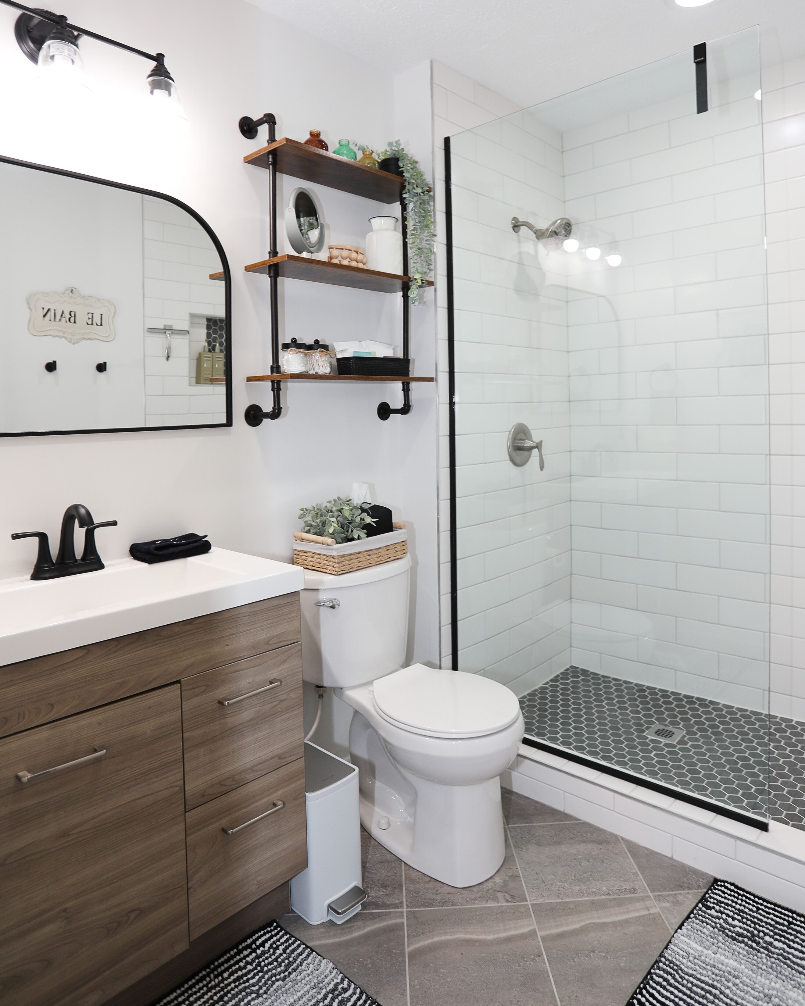 A modern bathroom with a white sink, wooden vanity, a toilet, and a glass-enclosed shower.
