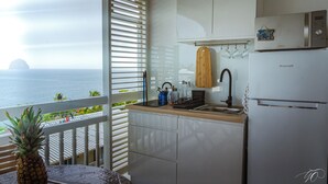 Une cuisine avec vue sur l’océan, un plan de travail en bois et un réfrigérateur de la marque Brandt.