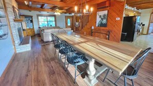 A spacious dining area with a long wooden table and black chairs, a chandelier, and a kitchen in the background. - Gorgeous Views and only 13 mi to Lost Maples SNA, 22 mi to Garner State Park! (Utopia)