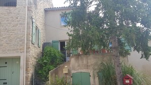 A narrow cobblestone street with a stone building featuring a green door and a small staircase leading to a second-floor window. - Location Maison de Village, vue Exceptionnelle (Grambois)