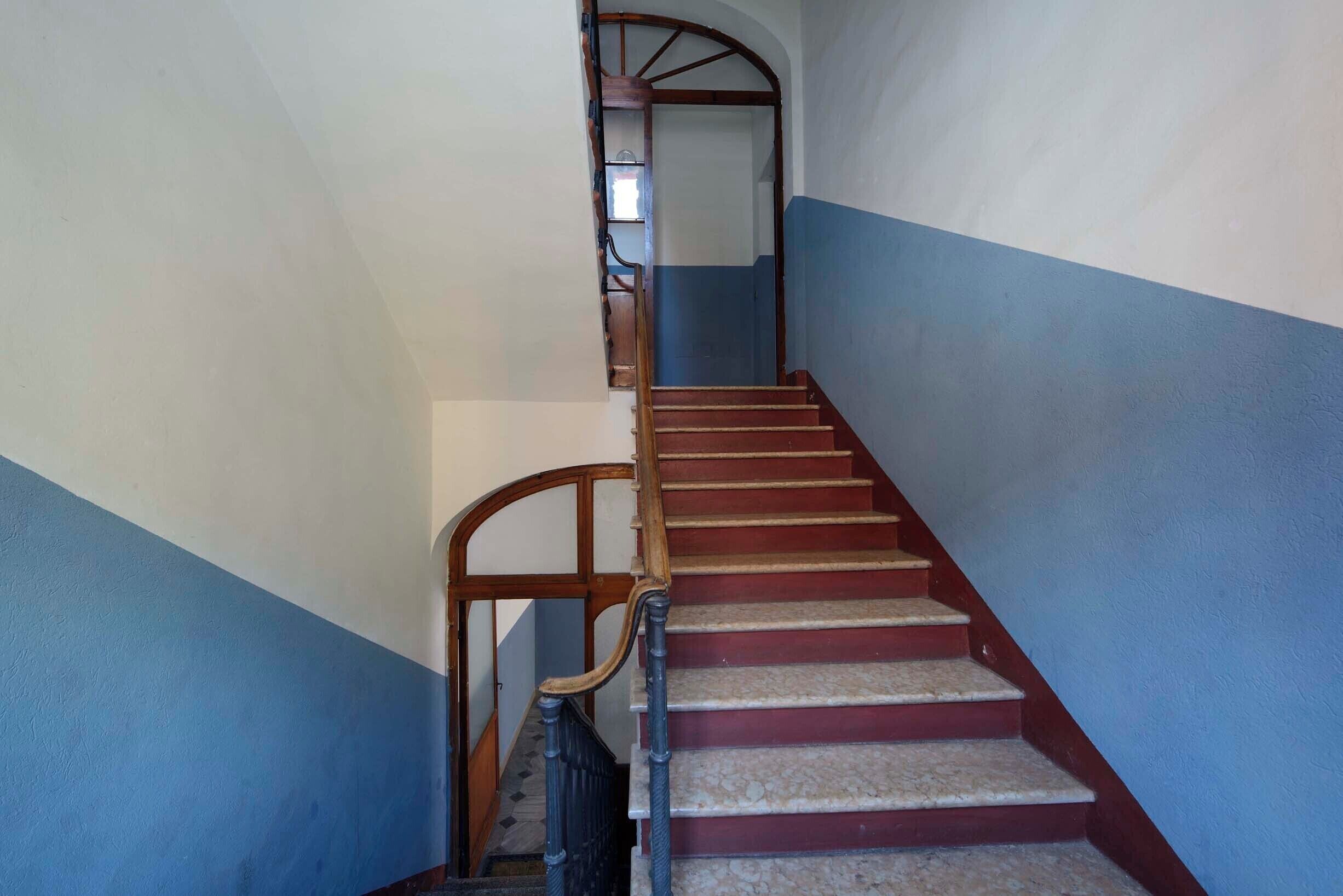 Eine Treppe mit Holzhandläufen und roten Stufen, die zu einer oberen Etage führt.