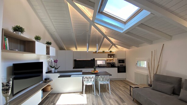 A modern kitchen with a skylight, a dining area with a white table and chairs, and a grey sofa. - GRENIER BLANC ELEGANT AND NEW ATTIC (San Pietro In Casale)