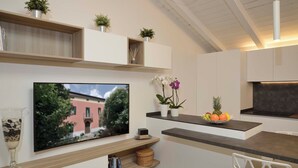 A modern kitchen with a built-in TV, wooden shelves, and a fruit bowl. - GRENIER BLANC ELEGANT AND NEW ATTIC (San Pietro In Casale)