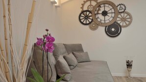 A modern living room with a grey sofa, decorative wall art, and a potted orchid plant. - GRENIER BLANC ELEGANT AND NEW ATTIC (San Pietro In Casale)