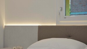 A bedroom with a bed, a bedside table with two candles, and a window with a view of a brick wall. - GRENIER BLANC ELEGANT AND NEW ATTIC (San Pietro In Casale)