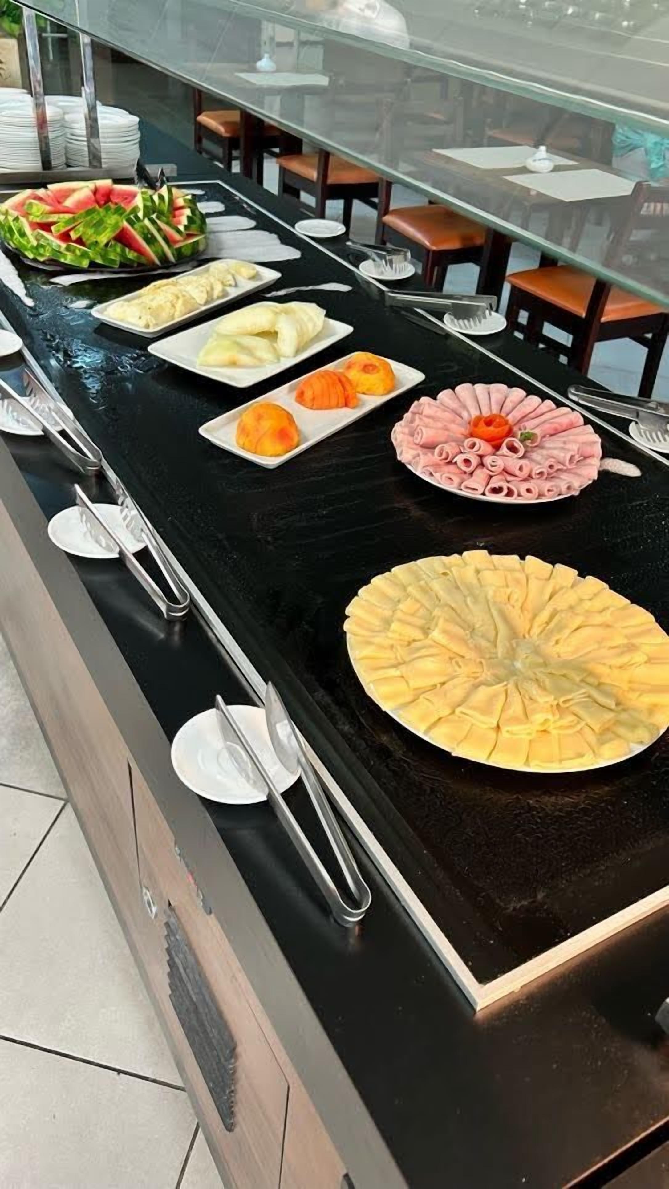 Un bufé con diversos platos, incluyendo sandía, pan y una amplia variedad de frutas.