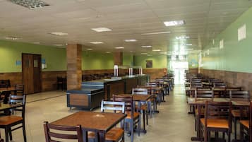 Uma cafeteria com mesas e cadeiras compridas, um balcão de atendimento central e paredes verdes.