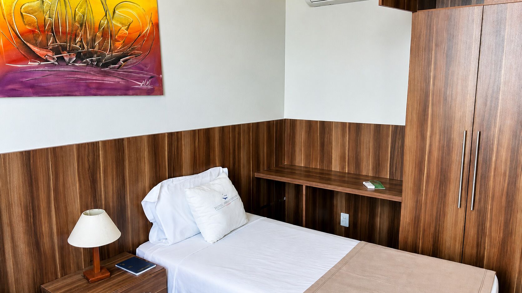 A hotel room with a bed, a nightstand, a lamp, a shelf, and a wardrobe.