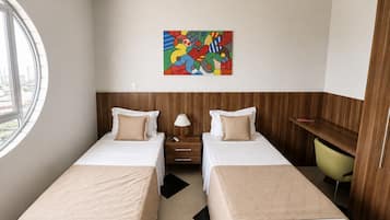 A hotel room with two beds, a desk, a chair, a lamp, and a colorful abstract painting on the wall.