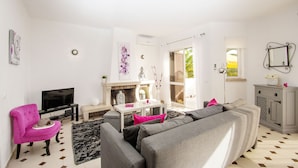 Ein modernes Wohnzimmer mit einem grauen Sofa, einem rosa Sessel, einem Flachbildfernseher und einem Kamin.