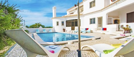 A pool area with lounge chairs, a hot tub, and a stone-tiled patio.