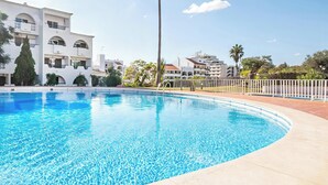 Una piscina con acqua cristallina, circondata da una recinzione bianca e moderni edifici sullo sfondo.
