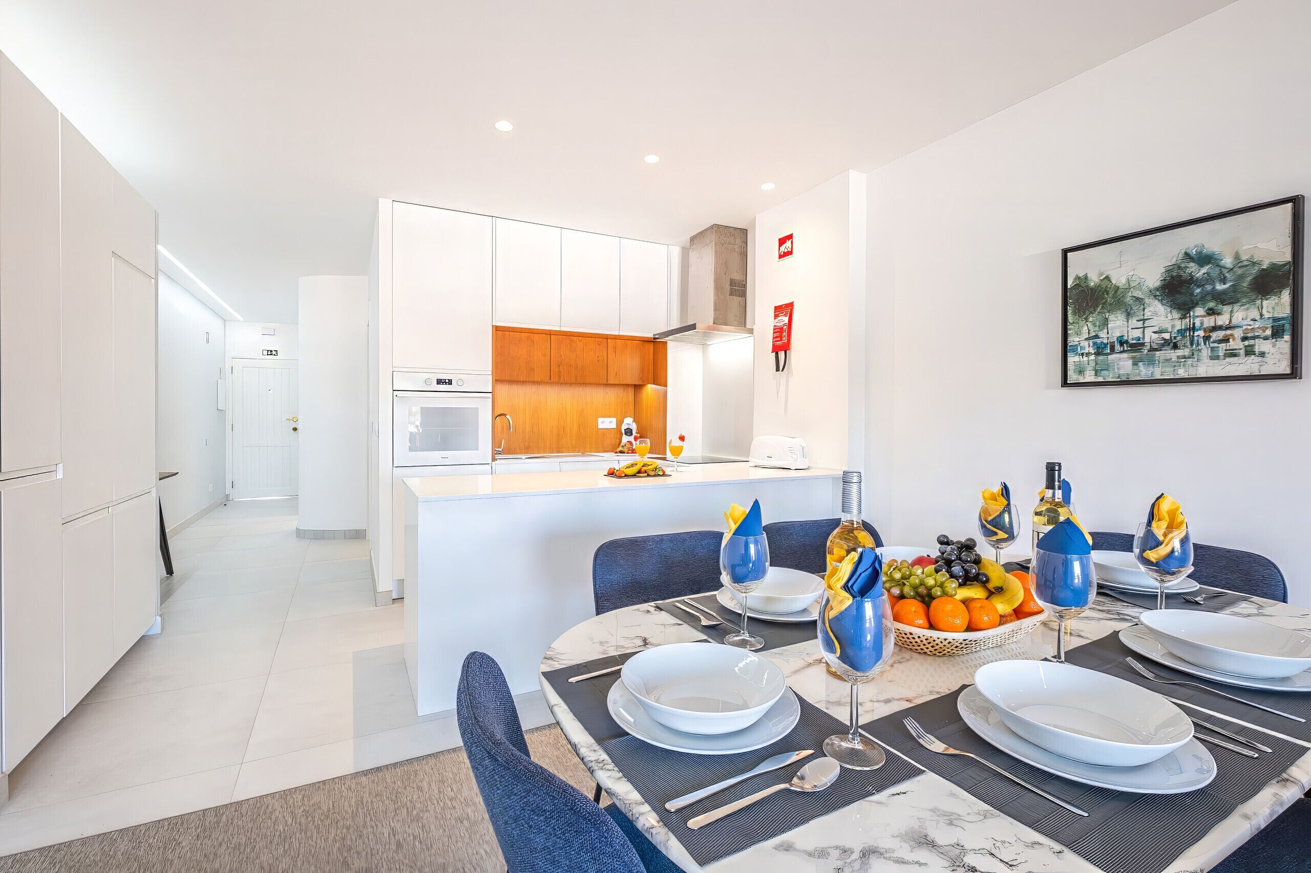 A modern kitchen with white cabinets, a marble countertop, and a dining area with a table set for four.