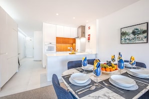 A modern kitchen with white cabinets, a marble countertop, and a dining area with a table set for four.