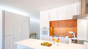 Una cucina moderna con mobili bianchi, una parete d'accento in legno, un forno integrato e un angolo per frutta e succhi.