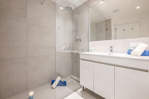 A modern bathroom with a glass-enclosed shower, a white vanity with a mirror, and a towel rack.