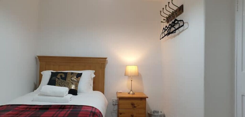 A neatly made bed with a wooden headboard, a bedside lamp, and a wall-mounted coat rack.