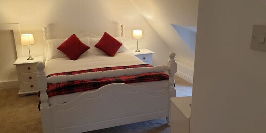 A white four-poster bed with red pillows, a plaid blanket, and two bedside lamps.