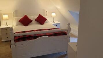 A white four-poster bed with red pillows, a plaid blanket, and two bedside lamps.