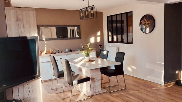 A modern kitchen with a dining area, a TV, and a large window.