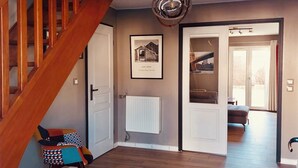 A staircase leading to a room with a radiator, a framed picture on the wall, and a view into another room with a sofa and a table.