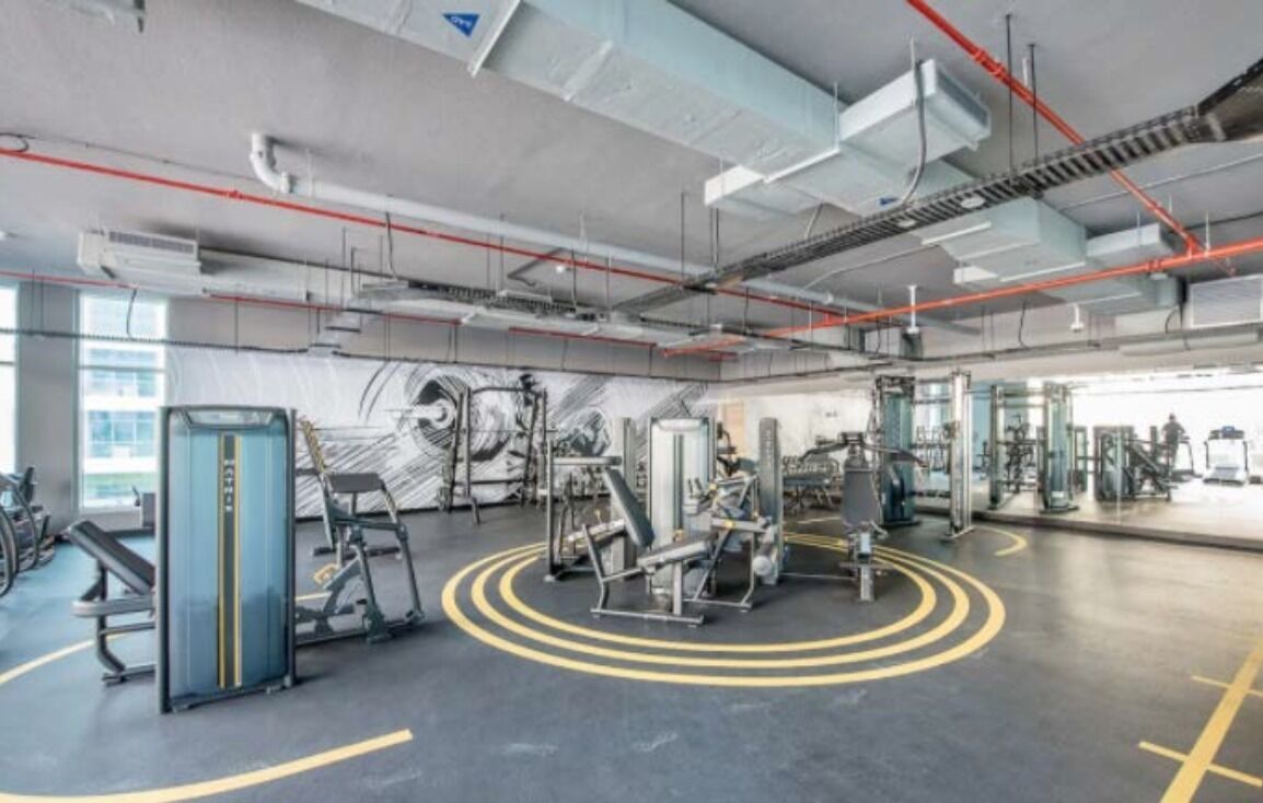 A gym with various exercise machines, a large mirror, and a circular yellow marking on the floor.