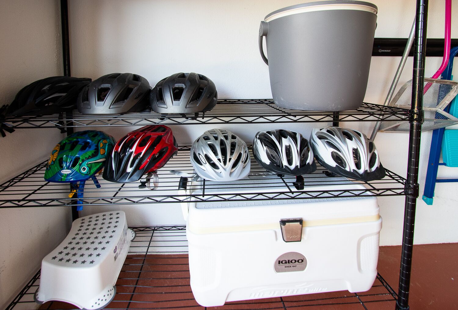A rack with various helmets and a white cooler with the brand IGIOO.