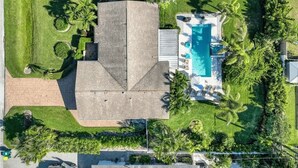 An aerial view of a residential property with a swimming pool, a large house, and surrounding greenery. - Three-bedroom home with backyard heated pool oasis. 5 minutes to the beach (Naples)