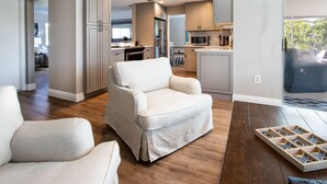 A modern living room with a sofa and a coffee table, a kitchen with appliances, and a view of the outdoors. - Three-bedroom home with backyard heated pool oasis. 5 minutes to the beach (Naples)