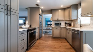 A modern kitchen with grey cabinets, stainless steel appliances, and a wooden floor. - Three-bedroom home with backyard heated pool oasis. 5 minutes to the beach (Naples)
