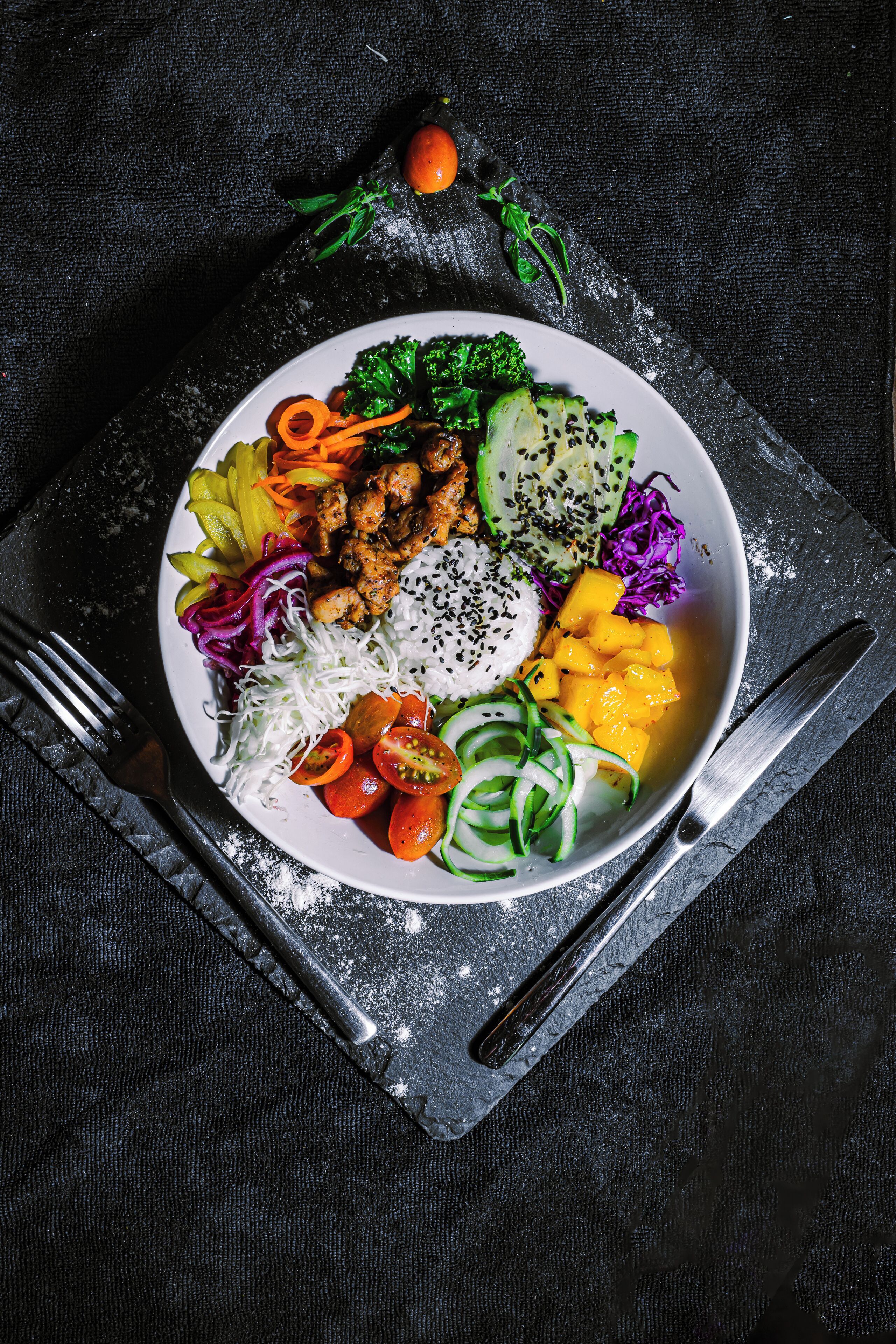 Un plato de comida con diversas verduras y un tazón blanco sobre una superficie oscura.
