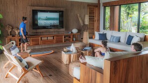 A modern living room with a large TV, wooden furniture, and a view of the outdoors. - Lamangata Luxury Surf Resort - All Inclusive (Savegre)
