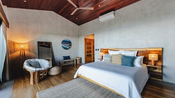 Un dormitorio con techo de madera, cama con ropa de cama blanca, espejo redondo en la pared y vista al mar.