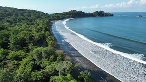 A beach with a curved shoreline, surrounded by dense green vegetation. - Lamangata Luxury Surf Resort - All Inclusive (Savegre)