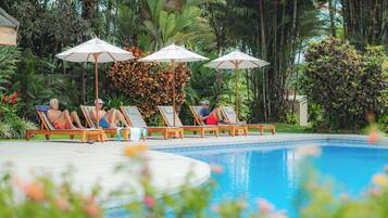 A poolside area with lounge chairs and umbrellas, surrounded by lush tropical vegetation.