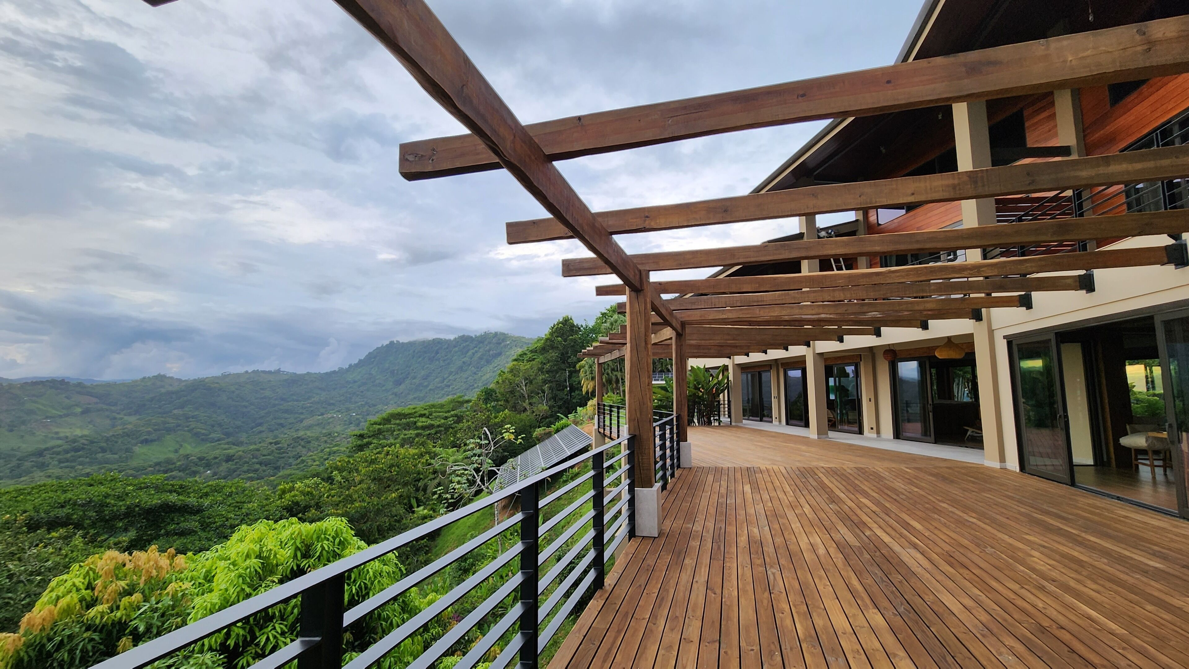 Um deck de madeira com guarda-corpo, com vista para um vale exuberante e montanhas.
